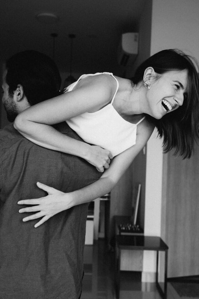A happy couple laughing indoors, captured in a black and white photo showcasing joy and love.